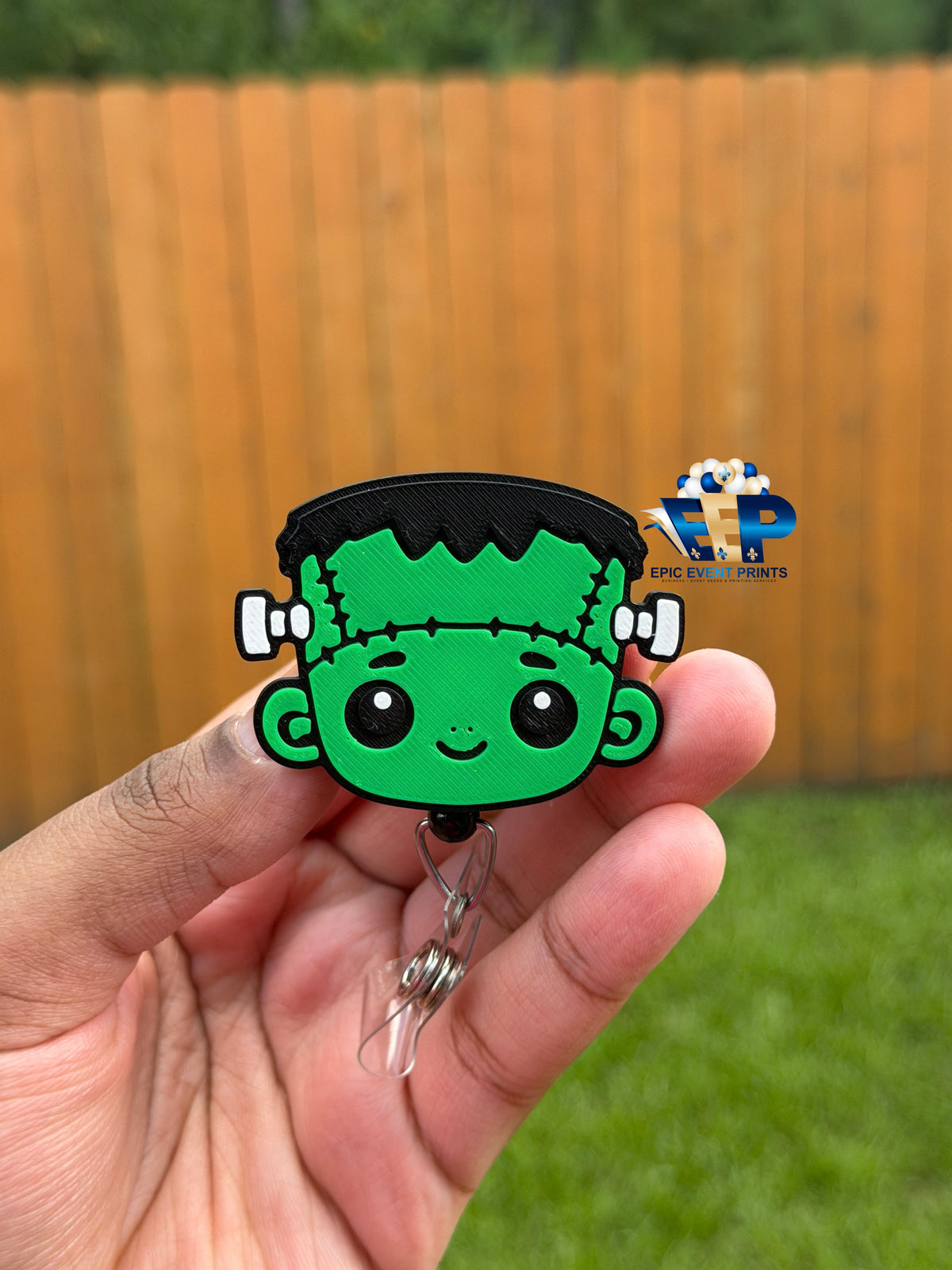 Green Frankenstein-inspired 3D badge reel with black hair and stitched details held in a hand