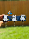 Three white ghost badge reels with bows and star accents displayed on a dark stand