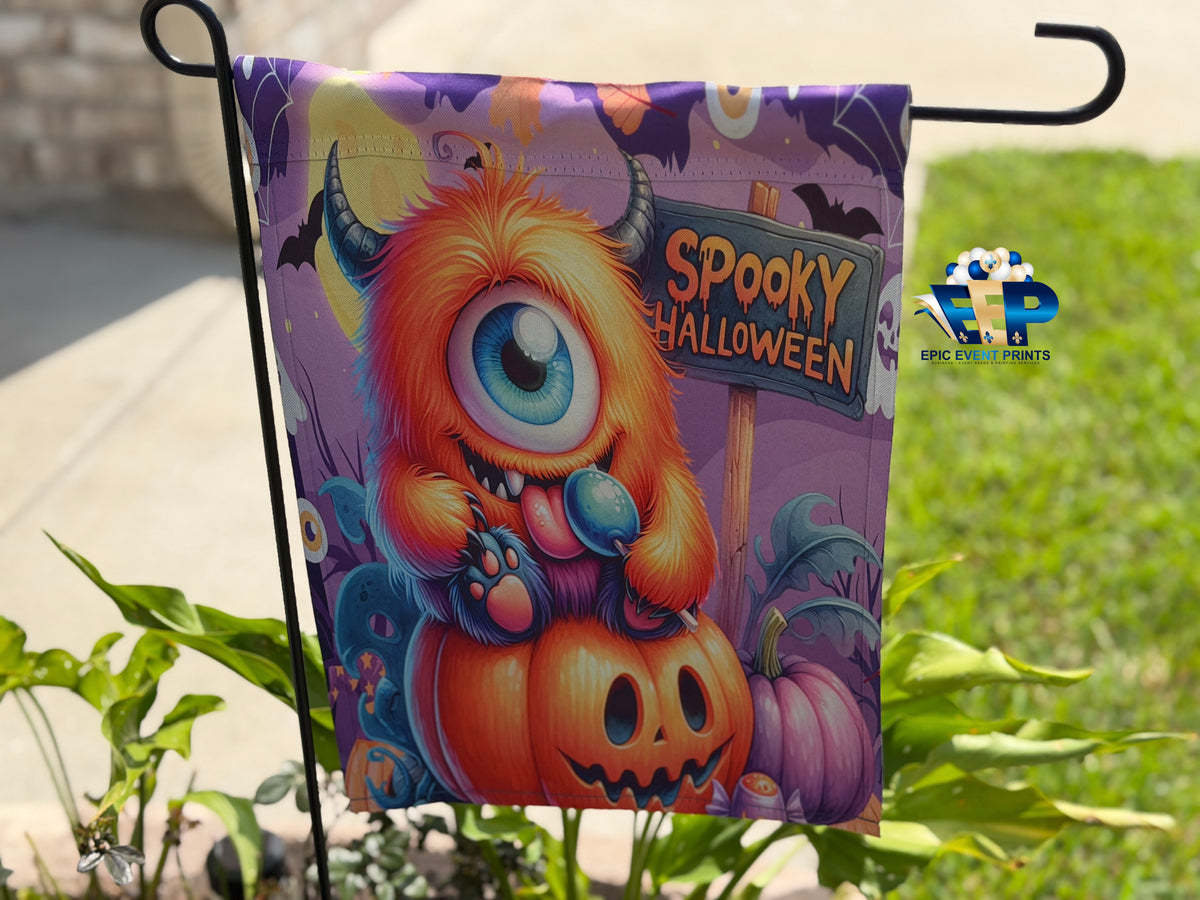 Orange one-eyed monster sitting on a jack-o'-lantern with pumpkins on a Halloween garden flag