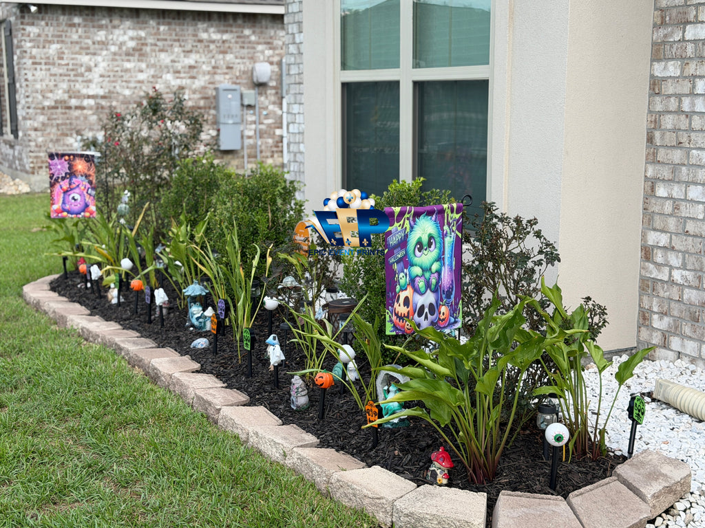 Halloween monster garden flags displayed in a landscaped flower bed outside a house