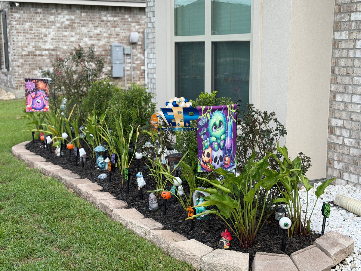 Halloween monster garden flags displayed in a landscaped flower bed outside a house